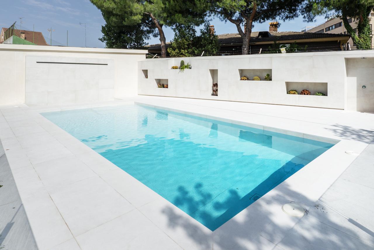 A white marble pool filled with inviting chlorinated water, a garden with a lawn and trees and niches with flower pots on one wall